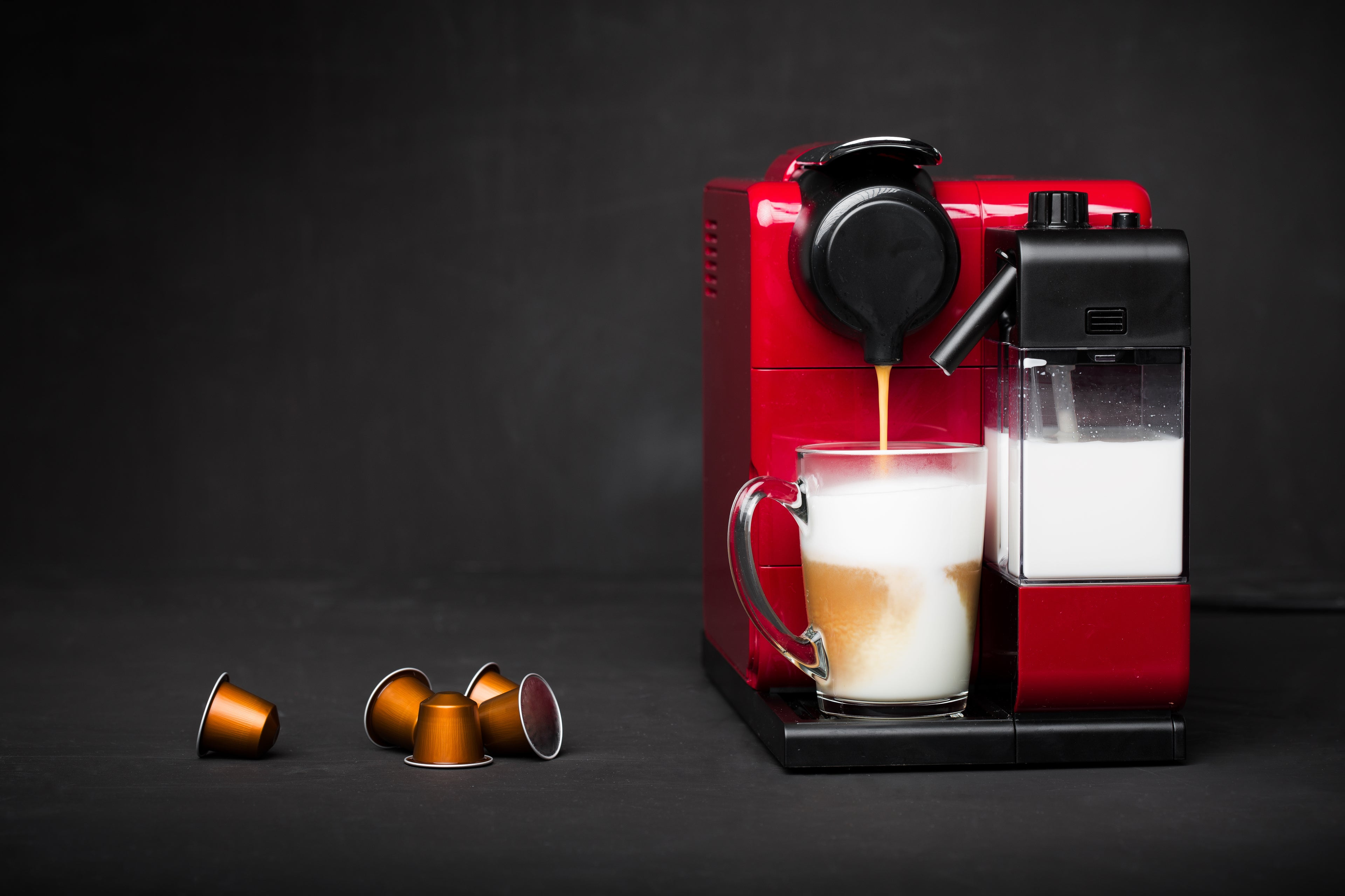 Red espresso machine making a cup of coffee with Nespresso capsules or pods on a dark background
